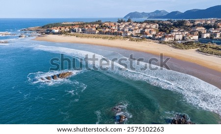 An aerial view of sandy Ris Beach, Atlantic Ocean waves, islets, Noja village, and distant mountains. Noja, Cantabria, Spain.