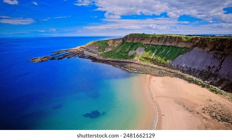 Aerial view of a scenic coastal landscape featuring a sandy beach, clear blue waters, and green cliffs under a partly cloudy sky. - Powered by Shutterstock