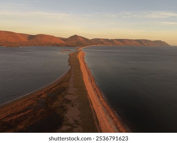 Aerial view of a scenic coastal landscape with a narrow sandbar and mountains at sunset, showcasing natural beauty and tranquility. - Powered by Shutterstock