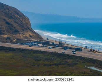 Aerial view of a scenic highway along San Diego's coast, with cars, a rugged cliff, and the expansive ocean. People are visible on the beach below. - Powered by Shutterstock