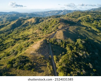 Aerial view of a scenic mountain landscape with a winding dirt road, lush greenery, and a clear blue sky. - Powered by Shutterstock