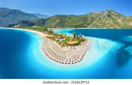 Aerial view of sea bay, sandy beach with umbrellas, trees, mountain at sunny day in summer. Blue lagoon in Oludeniz, Turkey. Tropical landscape with island, white sandy bank, blue water. Top view - Shutterstock ID 2156129715