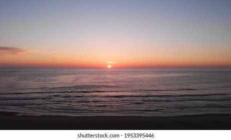 Aerial view of the sea, beach boulders and waves at sunset. Beautiful sunset with flying birds. Waves crashing on sandy beach. Beach with sand dunes and dusk sky in Ofir, Fao, Portugal.  - Powered by Shutterstock