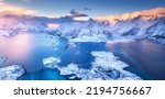 Aerial view of sea, snowy islands, mountains, road, sky with pink clouds at sunset in winter. Lofoten islands, Norway. Landscape with rocks in snow, water at dusk. Top view from above. Nature