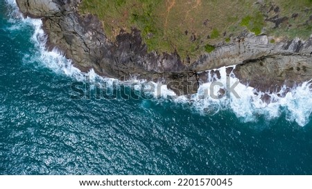 Aerial view of sea waves crashing on rocks cliff in the blue ocean. Top view of coastal rocks in Phuket ocean. Landscape view point of Laem Phromthep Cape in the morning.