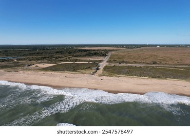 Aerial view of a serene beach with gentle waves and a vast landscape in the background under a clear blue sky. - Powered by Shutterstock