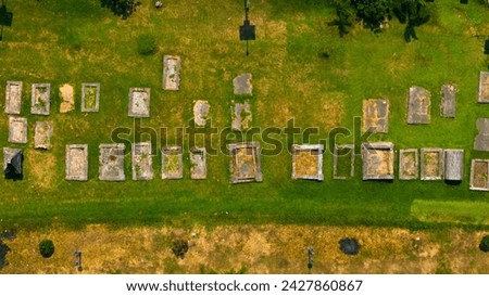 Aerial view of a serene cemetery with a patchwork of tombstones casting shadows over the lush grass, evoking a sense of peaceful finality