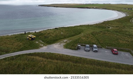 Aerial view of a serene coastal landscape with parked cars, a yellow van, and people enjoying the beach on a cloudy day. - Powered by Shutterstock