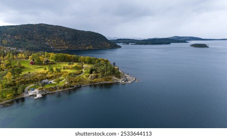 Aerial view of a serene coastal landscape featuring a calm sea, lush green hills, and scattered islands. The scene is adorned with autumn foliage, showcasing vibrant colors against a cloudy sky. - Powered by Shutterstock