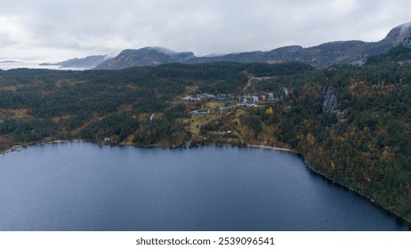 Aerial view of a serene lake surrounded by dense forest and mountains under a cloudy sky. With buildings on a hill near a lake - Powered by Shutterstock