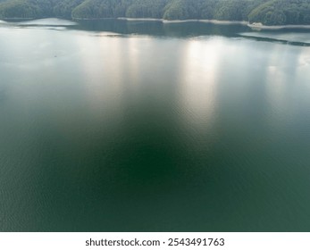 Aerial view of a serene lake surrounded by green mountains, showcasing calm waters reflecting the sky, perfect for nature lovers and tranquility seekers. - Powered by Shutterstock