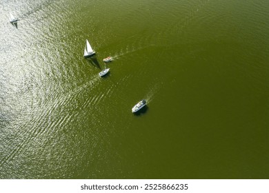 Aerial view of several boats sailing on a calm green lake under sunlight. A perfect day for sailing, showcasing nature's beauty and outdoor activities. - Powered by Shutterstock