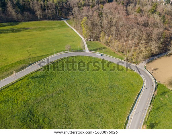 Aerial view of sharp hairpin curve\
of road through green meadow. Concept of traveling by\
car.