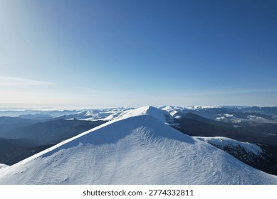 Aerial view of a sharp snow-covered mountain ridge under a clear blue sky