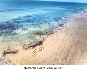 Aerial view of a shipwreck on a sandy beach with clear turquoise water and a blue sky. - Powered by Shutterstock