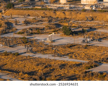 An aerial view shows numerous oil rigs in a grid pattern across a dry, arid California desert. Sparse vegetation and industrial structures are visible. - Powered by Shutterstock