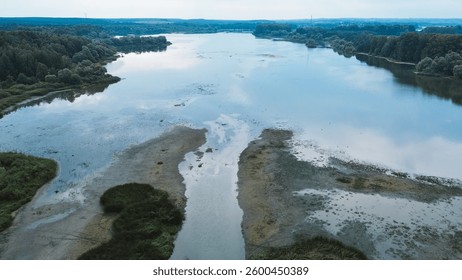 Aerial view of a shrinking river running through dried up cracked earth. The riverbed is drying up due to a severe drought