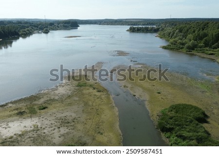 Aerial view of a shrinking river running through dried up cracked earth. The riverbed is drying up due to a severe drought