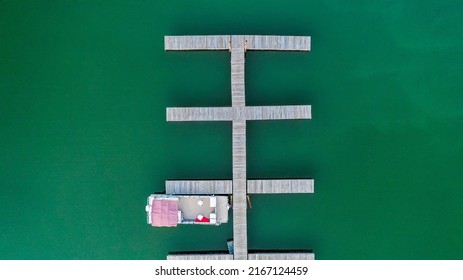 Aerial View Of A Single Pontoon Boat Moored At Floating Docks On Emerald Green Water.