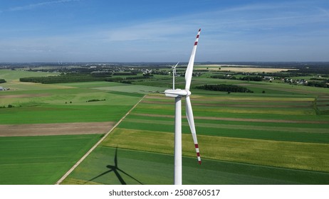 aerial view of a single wind turbine standing tall amidst expansive agricultural fields under a clear blue sky - Powered by Shutterstock