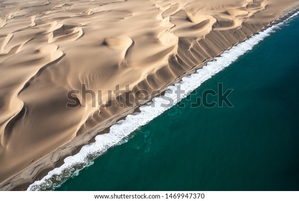 Aerial view of Skeleton\
coast sand dunes meeting the waves of Atlanic ocean. Skeleton\
coast, Namibia.