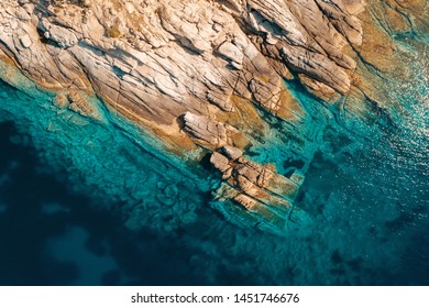 Aerial view of a slide turn from a drone on the view of calm turquoise sea water and rocks from molten lava. Pattern of sea surface and rocky shore. Thracian Sea, Greece. Rocky coast of the peninsula