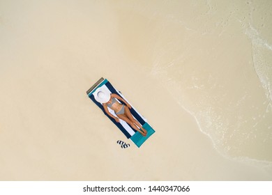 Aerial view of slim woman sunbathing lying on a beach chair in Maldives. Summer seascape with girl, beautiful waves, colorful water. Top view from drone.