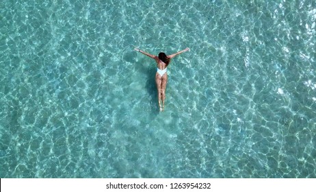 Aerial view of slim woman swimming in the transparent turquoise sea. Summer seascape with girl, beautiful waves, colorful water. Top view from drone