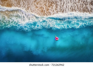 Воздушный вид стройной женщины, плавающие на розовом плавательном кольце в прозрачном бирюзовом море в Олюденизе, Турция. Летний морской пейзаж с девушкой, красивые волны, красочная вода на закате. Вид сверху с дрона