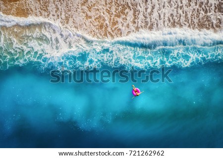 Aerial view of slim woman swimming on the pink swim ring in the transparent turquoise sea in Oludeniz,Turkey. Summer seascape with girl, beautiful waves, colorful water at sunset. Top view from drone