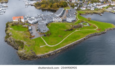 Aerial view of a small coastal village with modern houses, green lawns, and a playground, surrounded by water and rocky shores. - Powered by Shutterstock