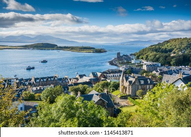 Aerial View Of Small Town Oban In Scotland. Scattered Trees, Small Village And Sea In The Background, Bright Sunny Day.