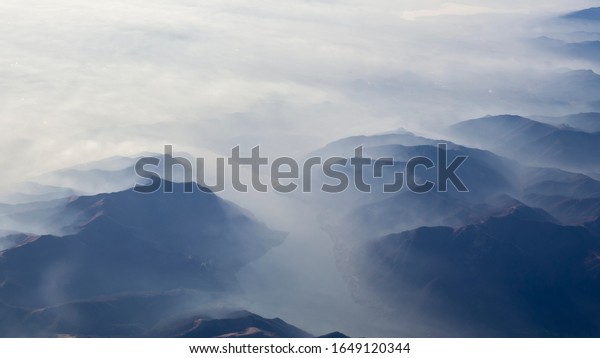 Aerial view of the\
smog and fog that covers the Po Valley in Italy and the first\
mountains of the Alps. Landscape from airplane window. Pollution\
due to low rain and no\
wind