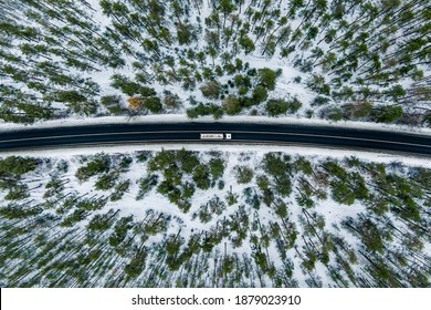 Aerial View Of Snow Covered Road In Winter Forest, Truck Driving By. Road Seen From The Air. Top View Landscape. Shooting From A Drone. Cargo Delivery In Winter