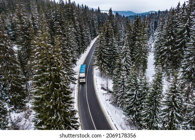 Aerial View Of Snow Covered Road In Winter Forest Blue Truck Driving By Road Seen From The Air. Top View Landscape. Shooting From A Drone. Cargo Delivery In Winter