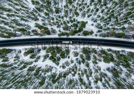 Aerial view of snow covered road in winter forest, truck driving by. Road seen from the air. Top view landscape. shooting from a drone. Cargo delivery in winter