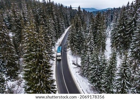 Aerial view of snow covered road in winter forest blue truck driving by road seen from the air. Top view landscape. shooting from a drone. Cargo delivery in winter