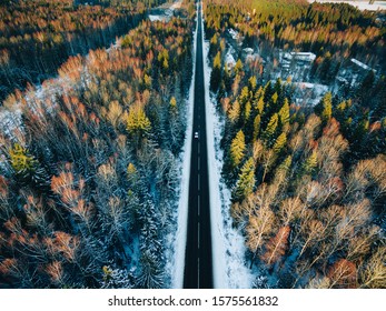 Aerial view of snow covered trees in the forest and winter country road with a car