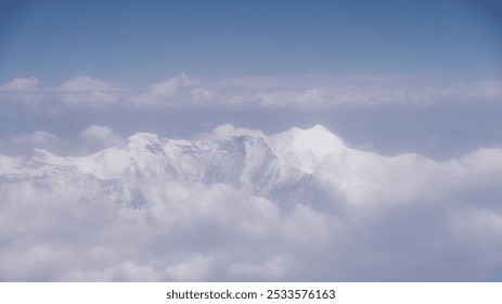 Aerial view of snow-capped mountains surrounded by clouds and a clear blue sky. - Powered by Shutterstock