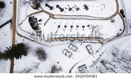 Aerial view of snow-clad tanks, artillery, and a jet fighter in Poznań Citadel during winter, shot by drone.