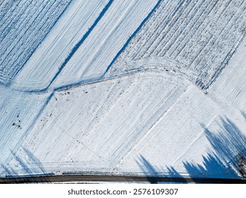 Aerial view of snow-covered fields with patterns and shadows, creating a tranquil winter landscape. Perfect for nature-themed projects and seasonal promotions.