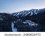 An aerial view of snowy, empty ski slopes and pine trees in Winter Park, Colorado at dusk