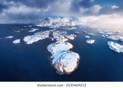 Aerial view of snowy Henningsvaer fishing village, Lofoten islands, Norway in winter at sunset. Top drone view of mountains in snow, sea, boats, cloudy sky, town, rorbuer and houses. Panorama. Scenery - Powered by Shutterstock