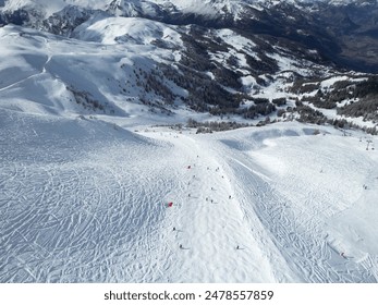 Aerial view of a snowy mountain landscape with skiers on the slopes, surrounded by forested hills. - Powered by Shutterstock