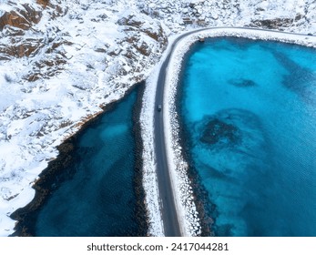 Aerial view of snowy road to the island and blue sea on both side. Bridge on snow and azure transparent water in winter. Landscape. Top drone view of road to the Henningsvaer, Lofoten islands, Norway - Powered by Shutterstock