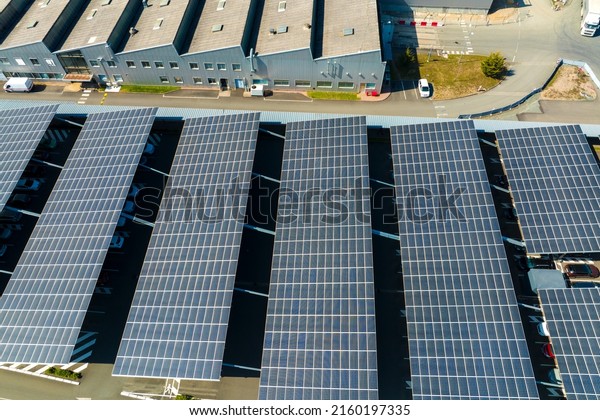 Aerial view of solar panels installed as\
shade roof over parking lot with parked cars for effective\
generation of clean electricity. Photovoltaic technology integrated\
in urban infrastructure