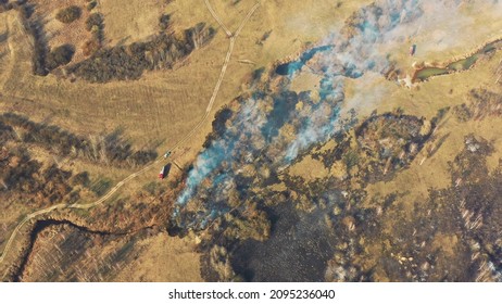 Aerial View. Spring Dry Grass Burns During Drought Hot Weather. Bush Fire And Smoke. Fire Engine, Fire Truck On Firefighting Operation. Wild Open Fire Destroys Grass. Ecological Problem Air Pollution.