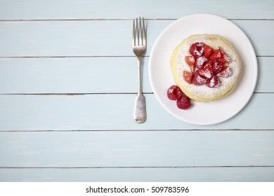Aerial view of a stack of berry covered pancakes on a blue wooden table background with blank space at side