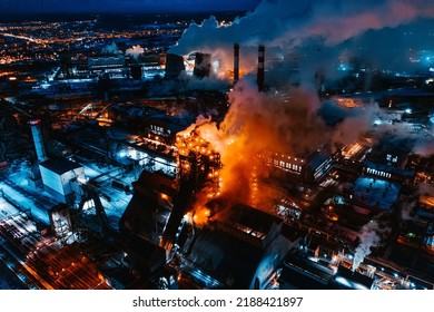 Aerial View Of Steel Plant At Night With Smokestacks And Fire Blazing Out Of The Pipe. Industrial Panoramic Landmark With Blast Furnance Of Metallurgical Production