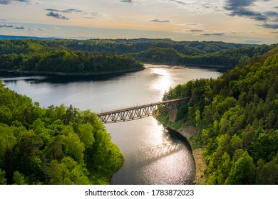 Aerial view of steel underspanned suspension railway bridge over Bobr River in Pilchowice, beautiful lake with islands and green forests in mountains on a sunny summer day in Pilchowice, Poland
